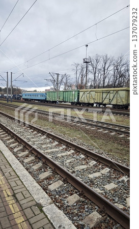 Railway tracks with freight train and passenger carriage at station under cloudy sky. Transportation and industrial logistics concept with cargo delivery and travel Railway tracks with freight train and passenger carriage at station under cloudy sky. Transportation and industrial logistics concept with cargo delivery and travel 137079232