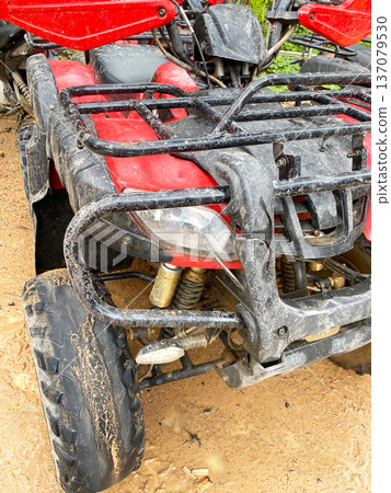 Close-up view of an all-terrain vehicle ATV featuring a rugged frame, exposed suspension components, and dirt-covered tires on a sandy surface in an outdoor setting 137079530