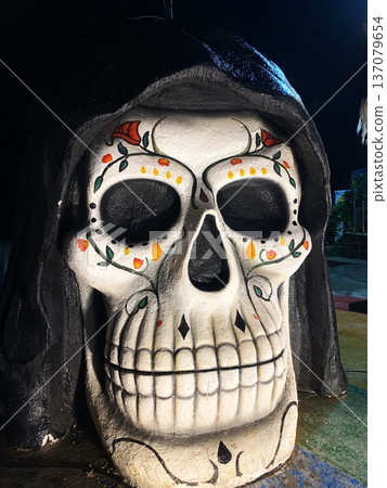 Large decorative skull with intricate floral patterns and vibrant colors, illuminated at night, showcasing Halloween-themed decor in a city center setting Large decorative skull with intricate floral patterns and vibrant colors, illuminated at night, showcasing Halloween-themed decor in a city center setting 137079654