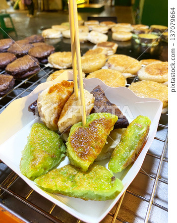 Coconut pancakes served in a white paper container with wooden skewers, featuring green and brown varieties, displayed at a street food stall in Asia 137079664