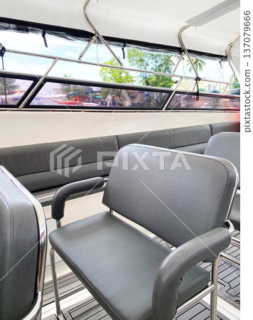 Empty seats on a tourist boat with gray cushioned chairs and large windows providing views of the surrounding landscape and natural light 137079666