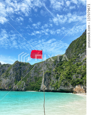 Red flag marking prohibited swimming area on Maya Bay Island, surrounded by lush green cliffs and clear turquoise waters under a bright blue sky Red flag marking prohibited swimming area on Maya Bay Island, surrounded by lush green cliffs and clear turquoise waters under a bright blue sky 137079671
