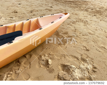 Orange kayak resting on sandy beach with visible footprints and textured sand, showcasing a tranquil outdoor setting ideal for water sports and recreation Orange kayak resting on sandy beach with visible footprints and textured sand, showcasing a tranquil outdoor setting ideal for water sports and recreation 137079692