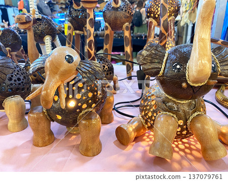 Handcrafted wooden elephant figurines with intricate cutouts and warm lighting displayed on a pink tablecloth at a handicraft market Handcrafted wooden elephant figurines with intricate cutouts and warm lighting displayed on a pink tablecloth at a handicraft market 137079761