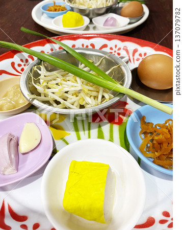 Ingredients for making classic Pad Thai displayed on colorful plates, including cabbage, eggs, garlic, and yellow tofu, arranged on a wooden table Ingredients for making classic Pad Thai displayed on colorful plates, including cabbage, eggs, garlic, and yellow tofu, arranged on a wooden table 137079782