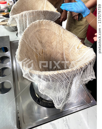 Traditional Thai cooking setup with muslin cloth draped over a steaming pot for preparing mango sticky rice dessert in a modern kitchen environment Traditional Thai cooking setup with muslin cloth draped over a steaming pot for preparing mango sticky rice dessert in a modern kitchen environment 137079789
