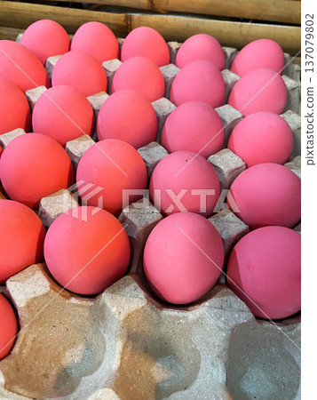 Pink dyed eggs arranged in a carton, showcasing vibrant colors and smooth surfaces, with a natural bamboo background enhancing the visual appeal of the scene 137079802