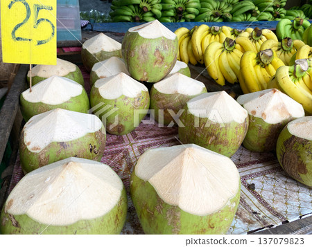 Fresh coconuts displayed for sale at an Asian market with a price sign, surrounded by ripe bananas in the background, showcasing vibrant colors and local produce 137079823