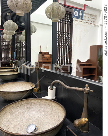 Asian-style toilet interior featuring multiple ceramic sinks with brass faucets, decorative lanterns, and wooden partitions in a modern restroom setting 137079828