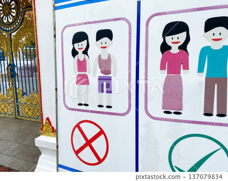 Warning sign at the entrance of a Thai temple displaying prohibited and permitted attire with illustrated figures and colorful graphics against a decorative background 137079834