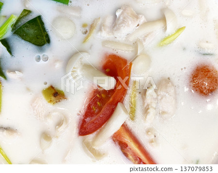 Close-up of coconut tom yum soup featuring chicken, mushrooms, tomatoes, and herbs in a creamy broth, highlighting vibrant ingredients and textures 137079853