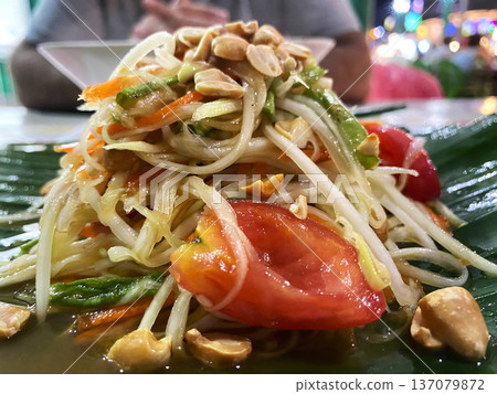 Pad Thai salad featuring shredded vegetables, peanuts, and tomatoes arranged on a banana leaf with a blurred background of a dining setting Pad Thai salad featuring shredded vegetables, peanuts, and tomatoes arranged on a banana leaf with a blurred background of a dining setting 137079872