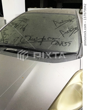 Dirty car windshield covered in dust and scratches with visible graffiti markings, showcasing a neglected vehicle parked in an indoor garage environment 137079942