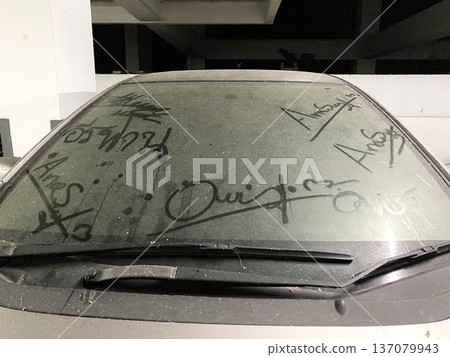Dirty car windshield with visible dust and markings, parked in a dimly lit garage with concrete structure and shadows in the background Dirty car windshield with visible dust and markings, parked in a dimly lit garage with concrete structure and shadows in the background 137079943