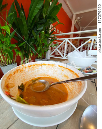 Empty bowl with remnants of soup and a spoon resting inside, surrounded by green plants and a bright orange wall in a modern dining setting Empty bowl with remnants of soup and a spoon resting inside, surrounded by green plants and a bright orange wall in a modern dining setting 137079960