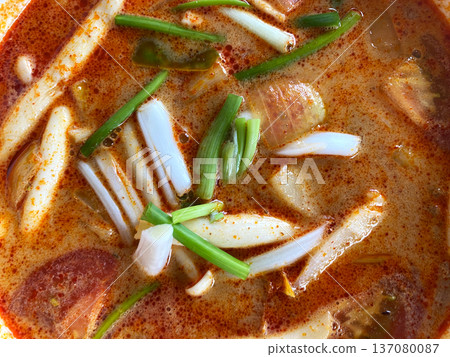 Close-up top view of vibrant tom yum soup featuring sliced mushrooms, green onions, and spices in a rich broth, served in a bowl with a colorful presentation 137080087