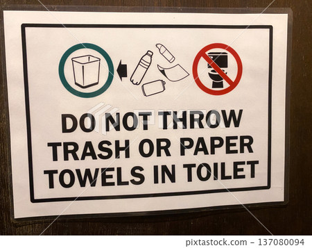 Sign instructing not to dispose of trash or paper towels in toilet, featuring icons for trash bin and prohibited items, displayed on a wooden door Sign instructing not to dispose of trash or paper towels in toilet, featuring icons for trash bin and prohibited items, displayed on a wooden door 137080094