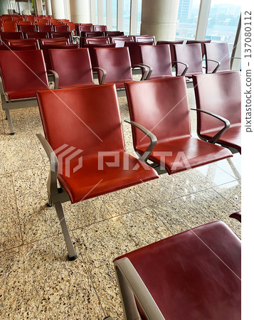 Red leather seating arrangement in a modern airport waiting area with polished granite flooring and large windows allowing natural light 137080112