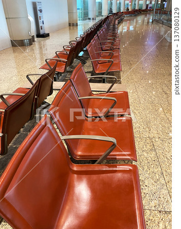 Rows of modern brown leather airport seating arranged in a waiting area with polished stone flooring and bright overhead lighting in a spacious terminal Rows of modern brown leather airport seating arranged in a waiting area with polished stone flooring and bright overhead lighting in a spacious terminal 137080129