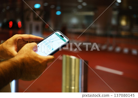 Person using smartphone app to call a taxi at the airport, illuminated surroundings with red flooring and blurred background elements visible Person using smartphone app to call a taxi at the airport, illuminated surroundings with red flooring and blurred background elements visible 137080145