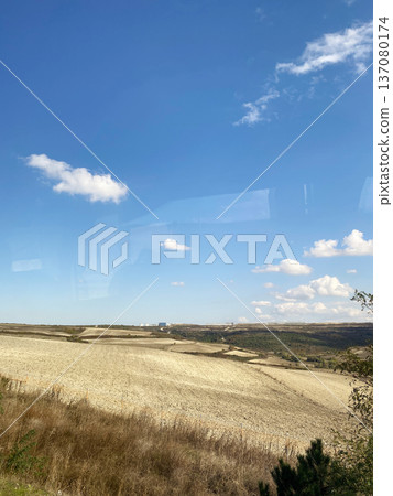 Scenic view of rolling fields and distant hills captured from a bus window in Turkey under a clear blue sky with scattered clouds Scenic view of rolling fields and distant hills captured from a bus window in Turkey under a clear blue sky with scattered clouds 137080174