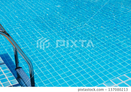 Swimming pool with clear blue water and tiled surface, featuring a stainless steel ladder on the side, creating a refreshing and inviting atmosphere for relaxation Swimming pool with clear blue water and tiled surface, featuring a stainless steel ladder on the side, creating a refreshing and inviting atmosphere for relaxation 137080213