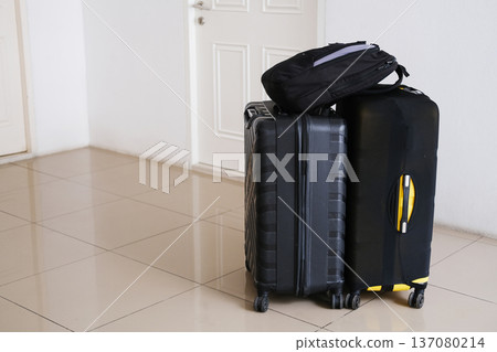 Two suitcases and a backpack stacked on a tiled floor inside an apartment entryway, with a white door visible in the background 137080214