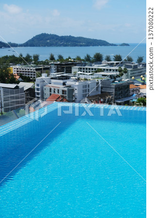 Rooftop swimming pool with clear blue water overlooking a coastal cityscape and distant island under a bright blue sky with scattered clouds 137080222