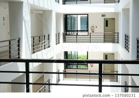 Modern multi-story building interior featuring open atrium with balconies, natural light streaming through large windows, and minimalist design elements visible throughout the space Modern multi-story building interior featuring open atrium with balconies, natural light streaming through large windows, and minimalist design elements visible throughout the space 137080231