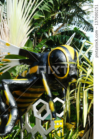 Close-up model of a bee sculpture with black and yellow colors surrounded by tropical plants in a garden setting, showcasing intricate details and textures Close-up model of a bee sculpture with black and yellow colors surrounded by tropical plants in a garden setting, showcasing intricate details and textures 137080251