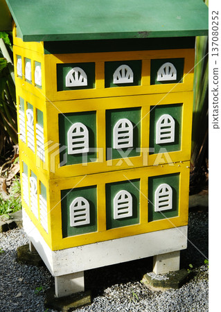 Beehive model designed as a fairytale house with colorful yellow and green exterior, featuring decorative windows and a sloped roof in a garden setting Beehive model designed as a fairytale house with colorful yellow and green exterior, featuring decorative windows and a sloped roof in a garden setting 137080252