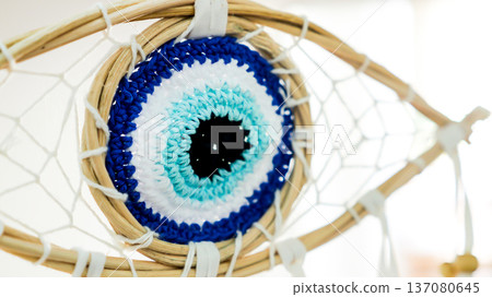 Crochet evil eye amulet integrated into a woven dreamcatcher, representing protection, spirituality, and good luck against negative energy and bad dreams with its intricate blue and white patterns Crochet evil eye amulet integrated into a woven dreamcatcher, representing protection, spirituality, and good luck against negative energy and bad dreams with its intricate blue and white patterns 137080645