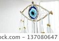 Handmade dreamcatcher amulet with an evil eye nazar woven from natural thread, accented with white feathers and wooden beads, hanging against a bright blue white backdrop 137080647