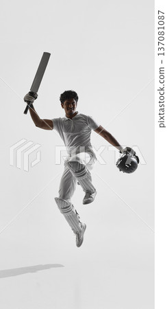 Cricket player jumping with bat raised in strong pose on white studio background wearing white uniform and pads. Cricket player jumping with bat raised in strong pose on white studio background wearing white uniform and pads. 137081087