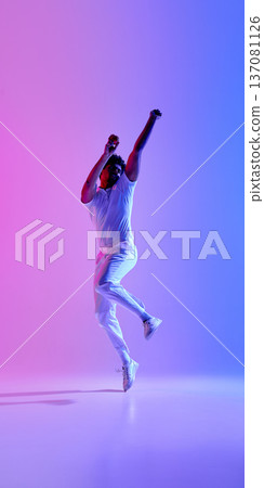 Cricket player jumping in white uniform under pink blue gradient lighting. Cricket player jumping in white uniform under pink blue gradient lighting. 137081126