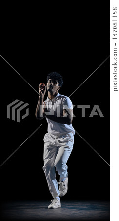 Cricket player holding red ball in ready position on dark background wearing white uniform Cricket player holding red ball in ready position on dark background wearing white uniform 137081158