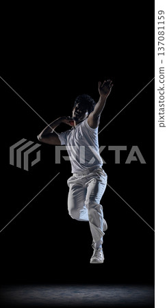 Cricket bowler preparing throw under dramatic lighting on dark background wearing white uniform. Cricket bowler preparing throw under dramatic lighting on dark background wearing white uniform. 137081159
