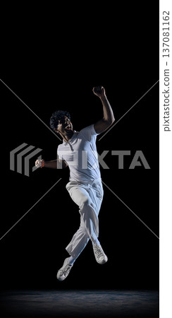 Cricket player celebrating mid air in spotlight on dark studio background wearing white uniform. Cricket player celebrating mid air in spotlight on dark studio background wearing white uniform. 137081162