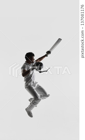 Cricket player jumping in air holding bat and helmet on white studio background in full white uniform. Cricket player jumping in air holding bat and helmet on white studio background in full white uniform. 137081176
