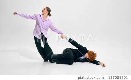 Businesswoman pulling colleague lying on floor in studio wearing formal office outfit on white background. Businesswoman pulling colleague lying on floor in studio wearing formal office outfit on white background. 137081201