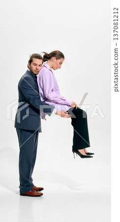 Businessman holding seated businesswoman working on laptop in studio wearing formal attire Businessman holding seated businesswoman working on laptop in studio wearing formal attire 137081212