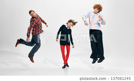 Three young adults jumping in coordinated studio fashion poses on white background. Three young adults jumping in coordinated studio fashion poses on white background. 137081245