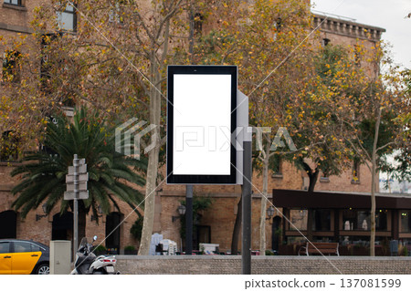 Blank vertical billboard mockup on a city street, displaying advertising copy space for urban marketing and branding in front of autumn trees and buildings 137081599