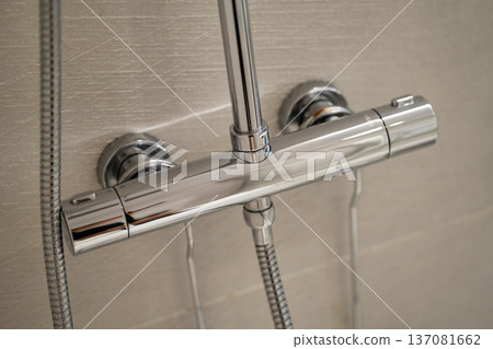 Chrome shower mixer tap on a light tiled bathroom wall, bringing modern design and functionality to the home for a refreshing and clean personal hygiene routine Chrome shower mixer tap on a light tiled bathroom wall, bringing modern design and functionality to the home for a refreshing and clean personal hygiene routine 137081662