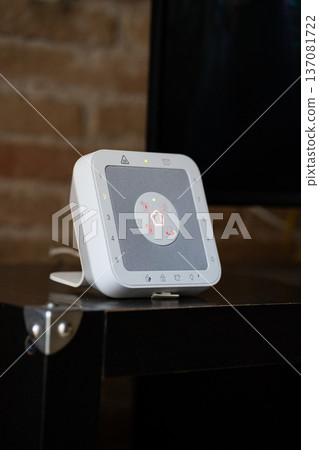 White smart home security hub displaying a central illuminated status light, integrating alarm system functions for modern house protection and automation White smart home security hub displaying a central illuminated status light, integrating alarm system functions for modern house protection and automation 137081722