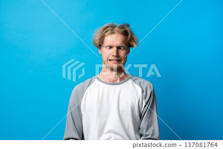 Man making a silly face and crossing eyes, expressing humor and a funny emotion with a goofy facial expression against a bright blue background 137081764