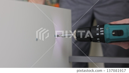 Professional man using an electric drill to adjust a wooden drawer. Furniture installation. Professional man using an electric drill to adjust a wooden drawer. Furniture installation. 137081917