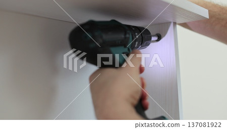 Close-up of person driving screw with cordless drill into furniture panel, assembling drawer. Close-up of person driving screw with cordless drill into furniture panel, assembling drawer. 137081922