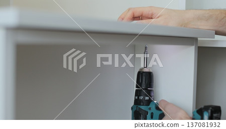 Close-up of person driving screw with cordless drill into furniture panel, assembling drawer. Close-up of person driving screw with cordless drill into furniture panel, assembling drawer. 137081932