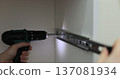 Man using a electric drill to attach a metal drawer slide to a piece of furniture during assembly. Furniture installation. 137081934